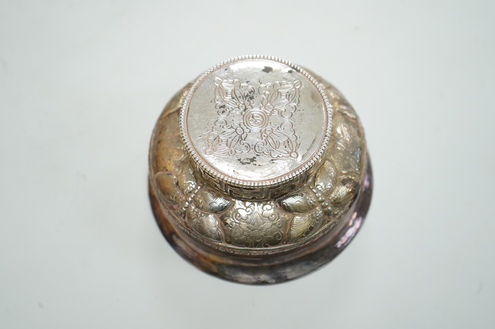 An antique Tibetan white metal mounted burl wood tsampa bowl, on a circular foot, diameter 99mm.